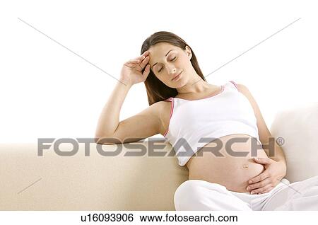 Stock Photograph - Pregnant young woman sitting on sofa, eyes closed, one hand on abdomen. Fotosearch
