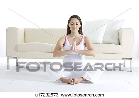 Stock Image - Pregnant young woman sitting on the floor in prayer position, in front of a sofa. Fotosearch