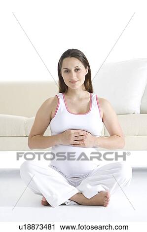 Pregnant young woman sitting cross-legged in front of a sofa, hands above the abdomen View Large Photo Image Stock Image - Pregnant young woman sitting cross-legged in front of a sofa, hands above the abdomen. Fotosearch