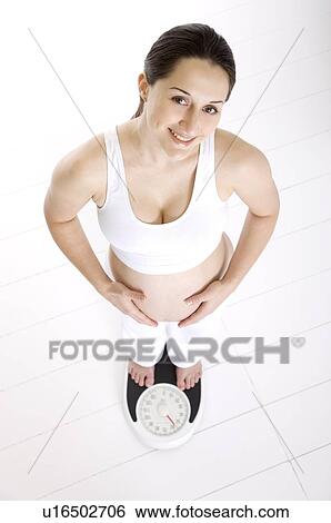 Pregnant young woman standing on a weighing scale, head back, looking up View Large Photo Image Stock Photograph - Pregnant young woman standing on a weighing scale, head back, looking up. Fotosearch