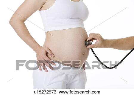 Stock Image - Pregnant young woman with a stethoscope on her abdomen, close-up. Fotosearch