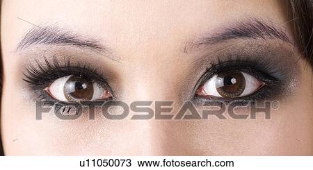 Stock Image - Close up of eyes applying smoked cosmetics. Fotosearch