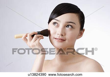Stock Image - Young women applying make-up with brush. Fotosearch