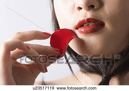 Stock Photo - Young women holding a petal under her red lips. Fotosearch