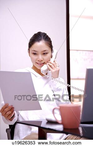Young woman on the phone looking at paper while working at home View Large Photo Image Stock Image - Young woman on the phone looking at paper while working at home. Fotosearch