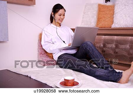 Stock Photo - Young woman sitting on floor using laptop. Fotosearch