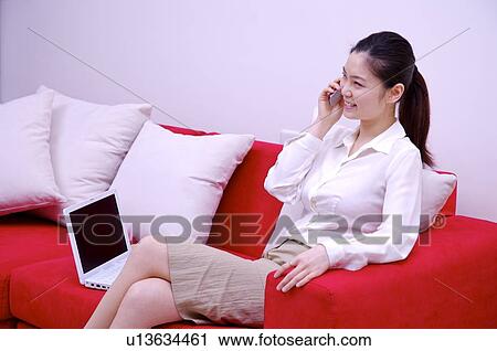 Young woman sitting on sofa using mobile phone View Large Photo Image Stock Image - Young woman sitting on sofa using mobile phone. Fotosearch