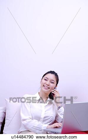 Young woman sitting on sofa using mobile phone and laptop View Large Photo Image Stock Image - Young woman sitting on sofa using mobile phone and laptop. Fotosearch