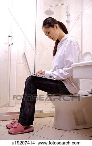 Young woman sitting on toilet using laptop View Large Photo Image Picture - Young woman sitting on toilet using laptop. Fotosearch