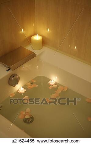 Stock Photography - Bathtub full of water and petals with burning candle on the edge. Fotosearch