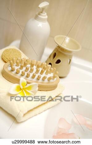 Stock Photo - Comb, frangipani and bath sponge on folded towel beside aromatherapy burner. Fotosearch