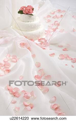 Stock Image - Wedding cake and rose petals on fabric. Fotosearch