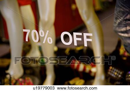 Stock Image - A discount sign on the window of a clothing store, in front of mannequins. Fotosearch
