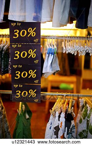 Stock Image - Black discount signs on the window of a clothing store, in front of racks of clothes. Fotosearch