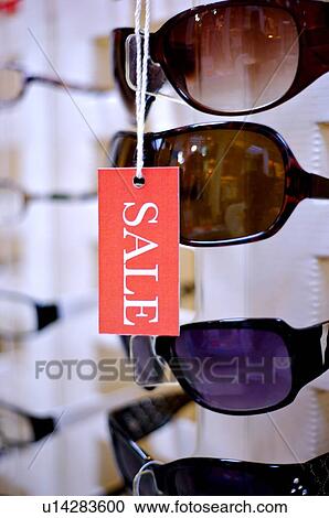 Stock Image - Close-up of a 'Sale' sign hanging in front of pairs of sunglasses. Fotosearch