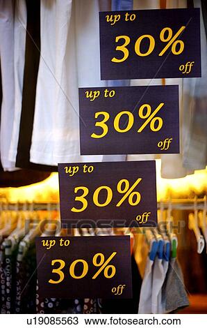 Stock Image - Discount signs on the window of a clothing store, in front of rows of clothes. Fotosearch