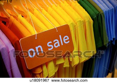 Stock Photo - Orange and white 'On Sale' sign in front of a row of colorful T-shirts. Fotosearch