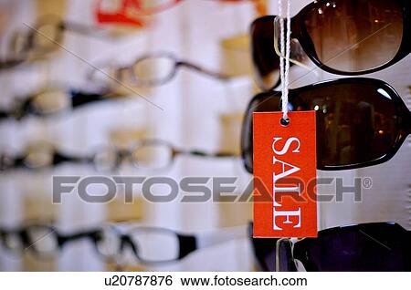Orange and white 'Sale' sign hanging in front of pairs of sunglasses in a store, close-up View Large Photo Image Stock Photograph - Orange and white 'Sale' sign hanging in front of pairs of sunglasses in a store, close-up. Fotosearch