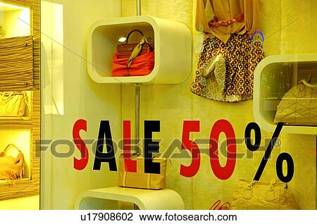 Stock Image - Red and black 'Sale' sign on the window of a store, with handbags and clothing in the display window. Fotosearch