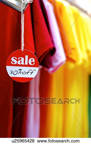 Stock Photo - Red and white discount sign hanging from a T-shirt, in front of a row of colorful T-shirts. Fotosearch