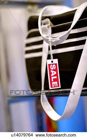 Picture - Red and white 'Sale' sign hanging from the strap of a black and white sports bag, selective focus. Fotosearch
