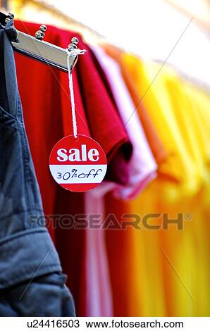 Red and white 'Sale' sign hanging from a clothes hanger, in front of a row of colorful T-shirts View Large Photo Image Stock Image - Red and white 'Sale' sign hanging from a clothes hanger, in front of a row of colorful T-shirts. Fotosearch