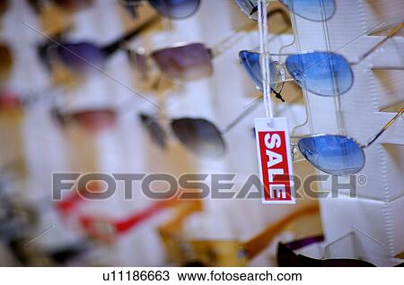 Stock Image - Red and white 'Sale' sign in front of a row of sunglasses. Fotosearch