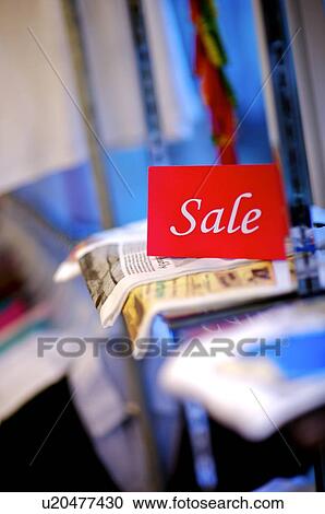 Stock Image - Red and white 'Sale' sign on top of clothes in a store, selective focus. Fotosearch