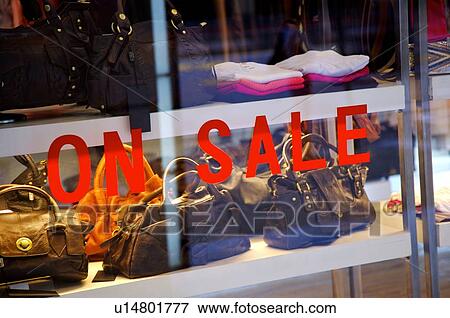 Stock Photo - Red 'On Sale' sign on the window of a store, with handbags in the display window. Fotosearch