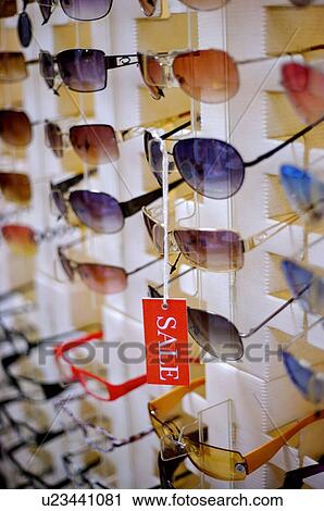 Stock Image - Red 'Sale' sign hanging from a pair of sunglasses, among rows of sunglasses, close-up. Fotosearch