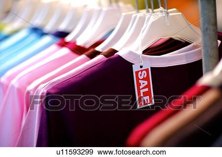 Stock Photo - Row of different colored T-shirts, with a small 'Sale' sign hanging from a T-shirt. Fotosearch