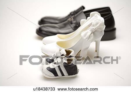 Stock Image - A pair of baby shoes, white high heels, and men's loafers, in a row. Fotosearch