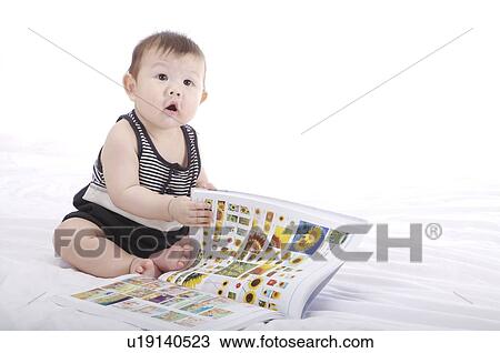 Stock Image - Baby boy flipping the pages of a colorful book, looking up. Fotosearch