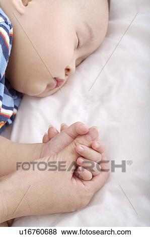 Baby boy holding his mother's hand, sleeping on his side, eyes closed View Large Photo Image Stock Photo - Baby boy holding his mother's hand, sleeping on his side, eyes closed. Fotosearch
