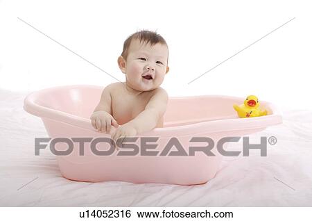 Stock Photograph - Baby boy sitting in a pink baby tub with a yellow rubber duck, laughing. Fotosearch