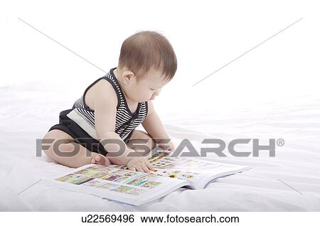 Stock Photograph - Baby boy sitting, looking at a picture book. Fotosearch