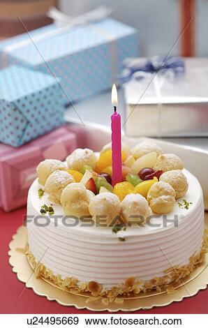 Birthday cake with a lighted candle on top, wrapped presents in the background View Large Photo Image Stock Photo - Birthday cake with a lighted candle on top, wrapped presents in the background. Fotosearch