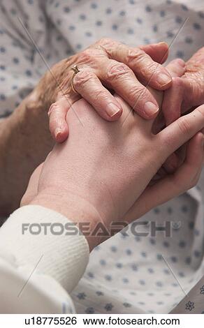 Stock Photograph - Senior woman in wheelchair holding hands with nurse. Fotosearch