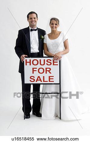 Stock Photography - Bride and groom holding house for sale sign. Fotosearch