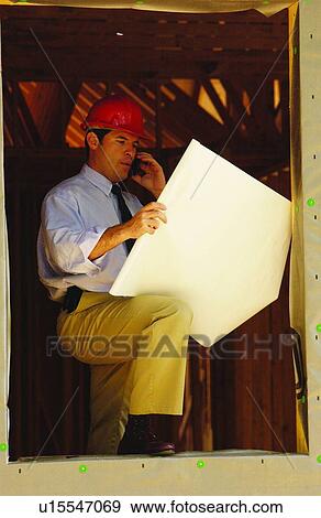 Contractor on cell phone looking over blueprints View Large Photo Image Stock Photo - Contractor on cell phone looking over blueprints. Fotosearch