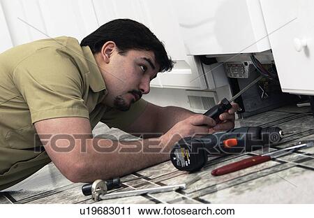 Stock Image - Man repairing dishwasher. Fotosearch