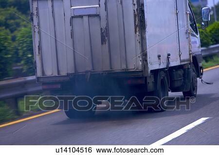Stock Photograph - Back of a truck on the road, with black smoke coming out from behind the truck. Fotosearch