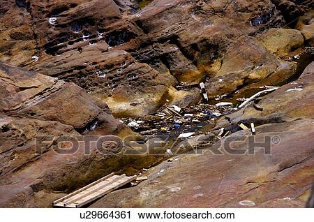 Stock Image - Garbage floating on a stream between large rocks. Fotosearch