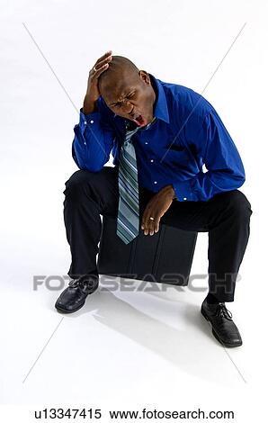 Stock Photography - African American businessman sitting on briefcase. Fotosearch