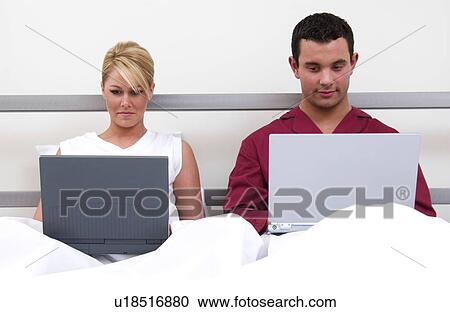 Stock Image - Couple in bed working on laptop computers. Fotosearch