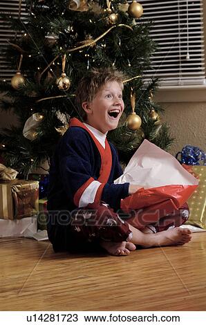 Boy near Christmas tree opening gifts View Large Photo Image Stock Image - Boy near Christmas tree opening gifts. Fotosearch