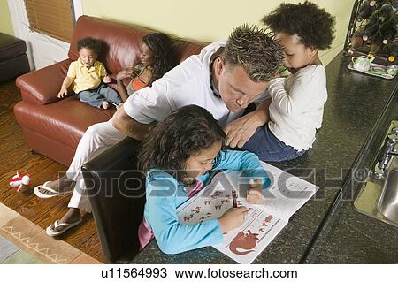 Stock Image - Caucasian dad helping 6 year old Mulatto girl with her arithmetic. 1. 5 year Mulatto boy with AA mom on sofa. 3 year old girl with dad on counter.. Fotosearch