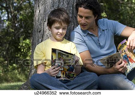 Father and son beside tree reading comic books, Assiniboine Park, Winnipeg, Canada View Large Photo Image Stock Image - Father and son beside tree reading comic books, Assiniboine Park, Winnipeg, Canada. Fotosearch