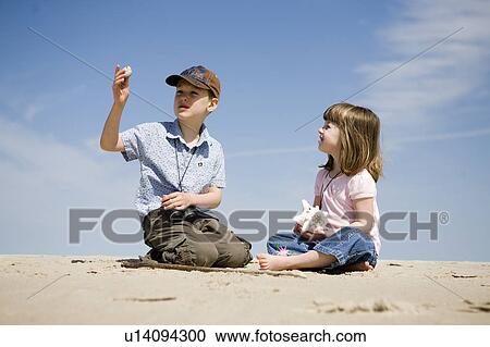 Stock Image - Four year old girl and seven year old boy look at shells, Grand Beach Provincial Park, Manitoba, Canada. Fotosearch