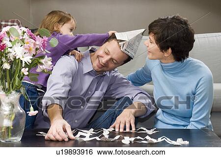 Stock Photograph - Using newsprint for kids games; child grabs at newsprint hat while man plays with newsprint paper dolls, Winnipeg, Canada. Fotosearch